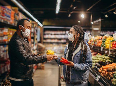 Woman smiling while holding a reusable grocery bag full of fresh produce.